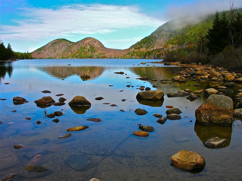 Jordan Pond shoreline with calm water, smooth granite rocks, and fall foliage in Acadia National Park