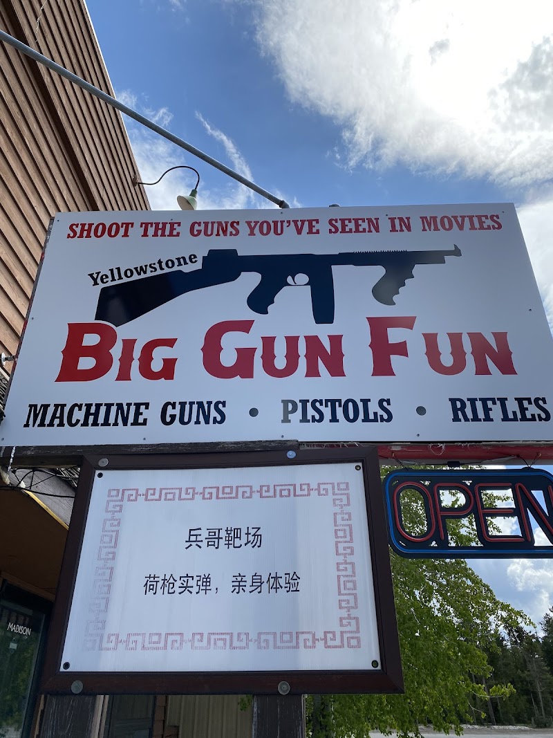 Gift shop sign at Yellowstone National Park features a black rifle silhouette and bold red 'Big Gun Fun' lettering, with an OPEN sign nearby.