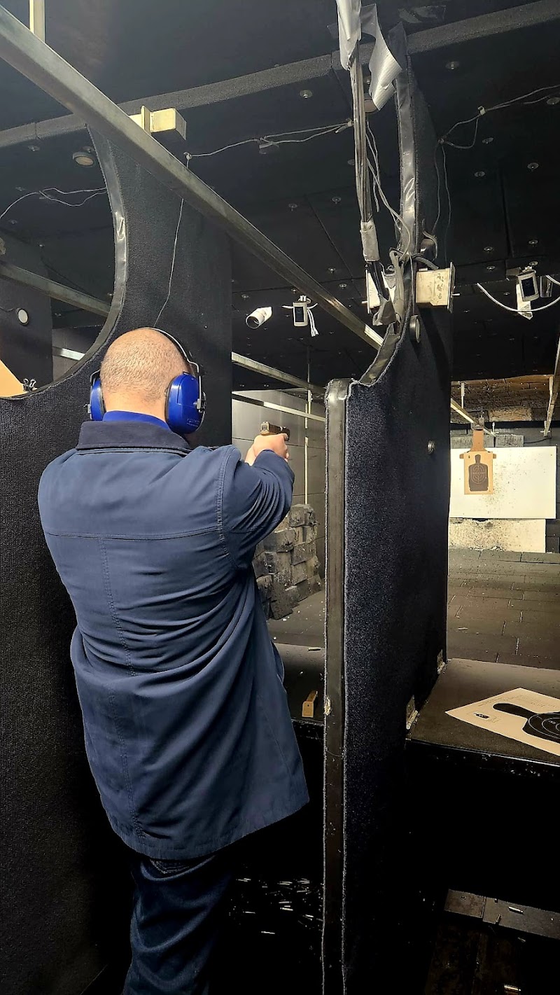 Inside a dim shooting range with black dividers, a man wearing blue ear protection fires a pistol from a booth in Yellowstone National Park.