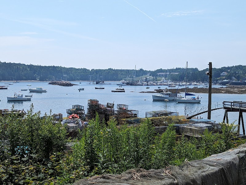 Harbor scene at Acadia National Park with small boats, lobster pots, a wooden pier, and seaweed-lined foreground.