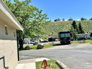 Yellowstone National Park campground scene with RVs, a small building, trees, and a grassy hillside.