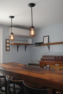 Cozy bar interior with a polished wooden counter, two rustic pendant lights, and glass racks in Acadia National Park.