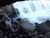 Cave Falls roars over jagged rocks while a hiker stands near the water’s edge in Yellowstone National Park.