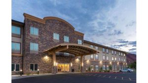 Exterior of a stone hotel with a curved wooden canopy, lit entry, and parking lot near Arches National Park.
