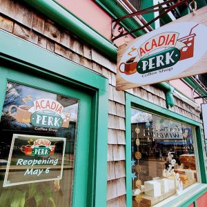 Green-framed storefront with wooden shingles in Acadia National Park, showing coffee shop signage and a window display.