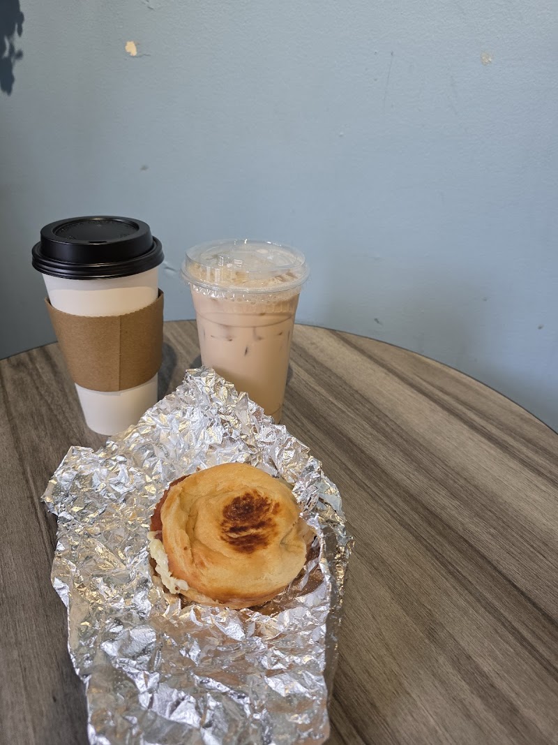 Hot coffee to-go, iced coffee in a plastic cup, and a foil-wrapped pastry on a wooden table at Acadia National Park.