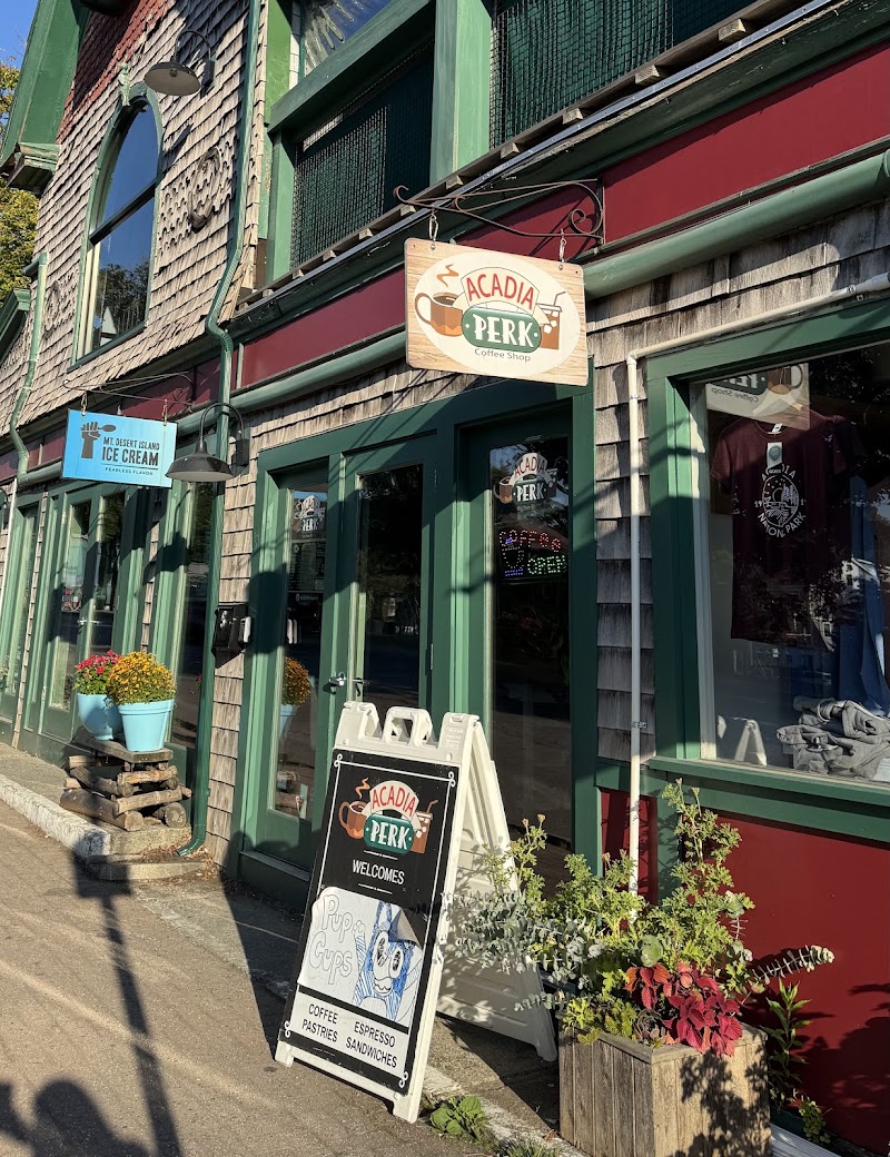 Colorful storefront with green trim and shingled facade, coffee shop sign, chalkboard menu, and potted plants outside in Acadia National Park.