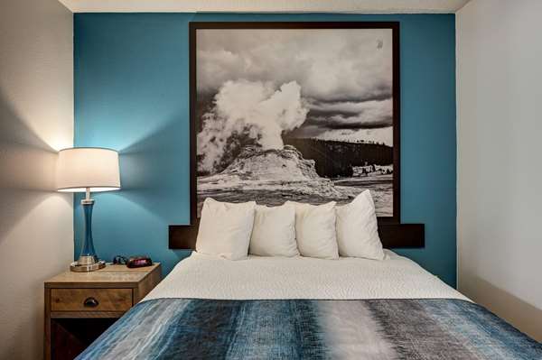 Cozy hotel room in Yellowstone National Park featuring a queen bed, white bedding, pillows, blue accent wall, and image.