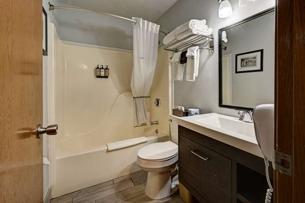 Hotel bathroom features a tub/shower with curtain, toilet, dark wood vanity, mirror and towels, Yellowstone National Park.