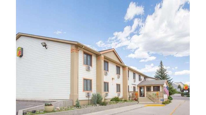 Two-story beige motel building with white trim, entrance stairs, an American flag, and a parking lot near Yellowstone National Park.