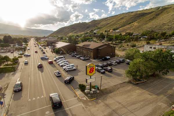 Busy main street with a motel row, parked cars, and a sign beside brown buildings, set against grassy hills in Yellowstone