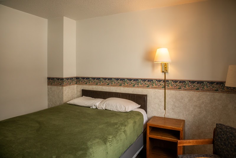 Cozy hotel room with green bedspread, two pillows, wooden nightstand, and wall lamp in Badlands National Park.
