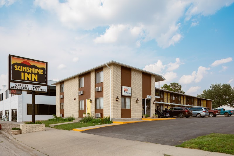 Two-story beige and brown motel with a large roadside sign, parked cars, and a bright blue sky at Badlands National Park.