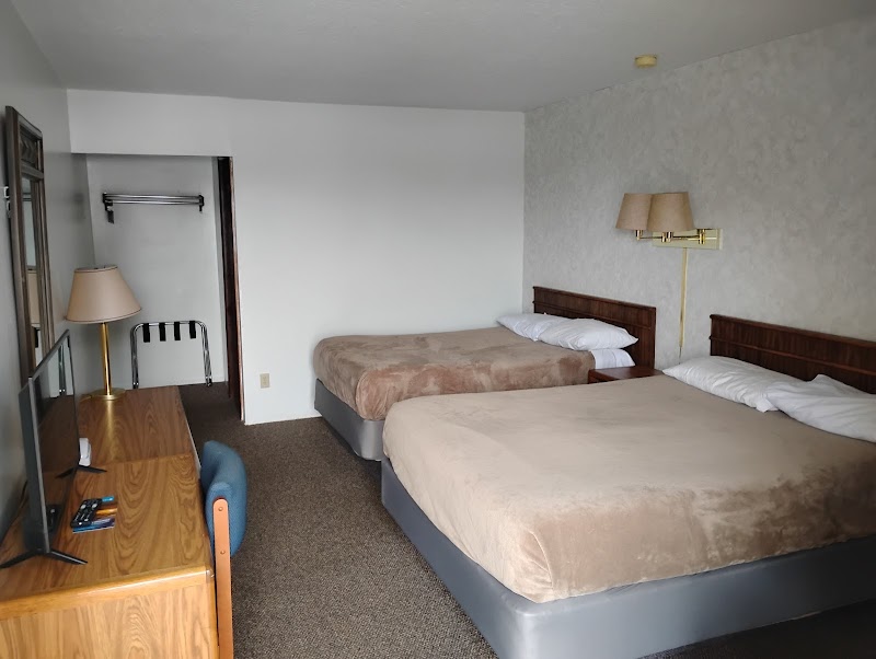 Two queen beds with beige duvets and wooden headboards in a carpeted hotel room at Badlands National Park, plus dresser, desk, TV, and open closet.