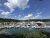 Boats and sailboats docked along a calm harbor at Mount Desert in Acadia National Park, with a blue sky and green hills in the background.