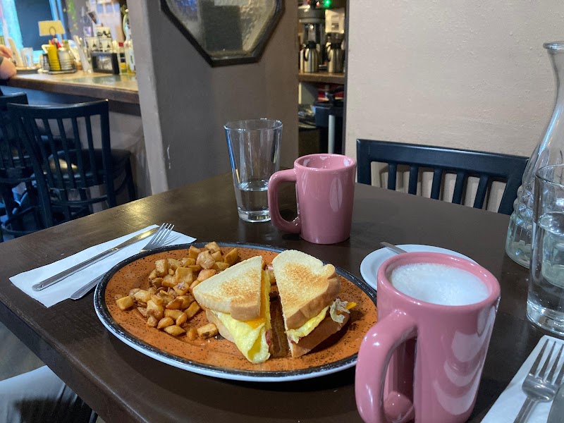 Casual cafe scene in Yellowstone National Park with a plate of eggs, toast, and home fries alongside pink mugs on a dark table.