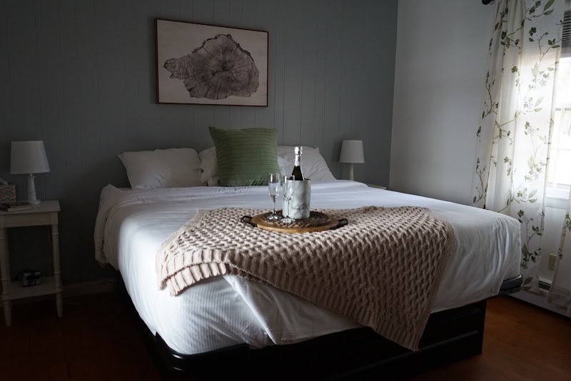 Cozy lakeside inn room in Acadia National Park with a white bed, pale green throw pillow, and a knitted cream blanket at the foot.