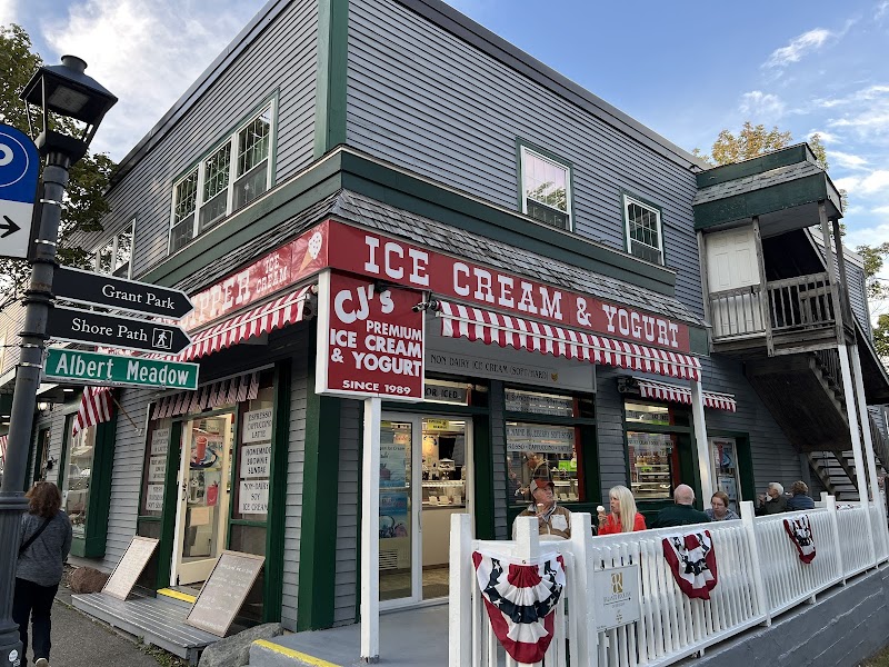 Two-story gray building with a red-and-white striped awning and outdoor seating behind a white fence in Acadia National Park.