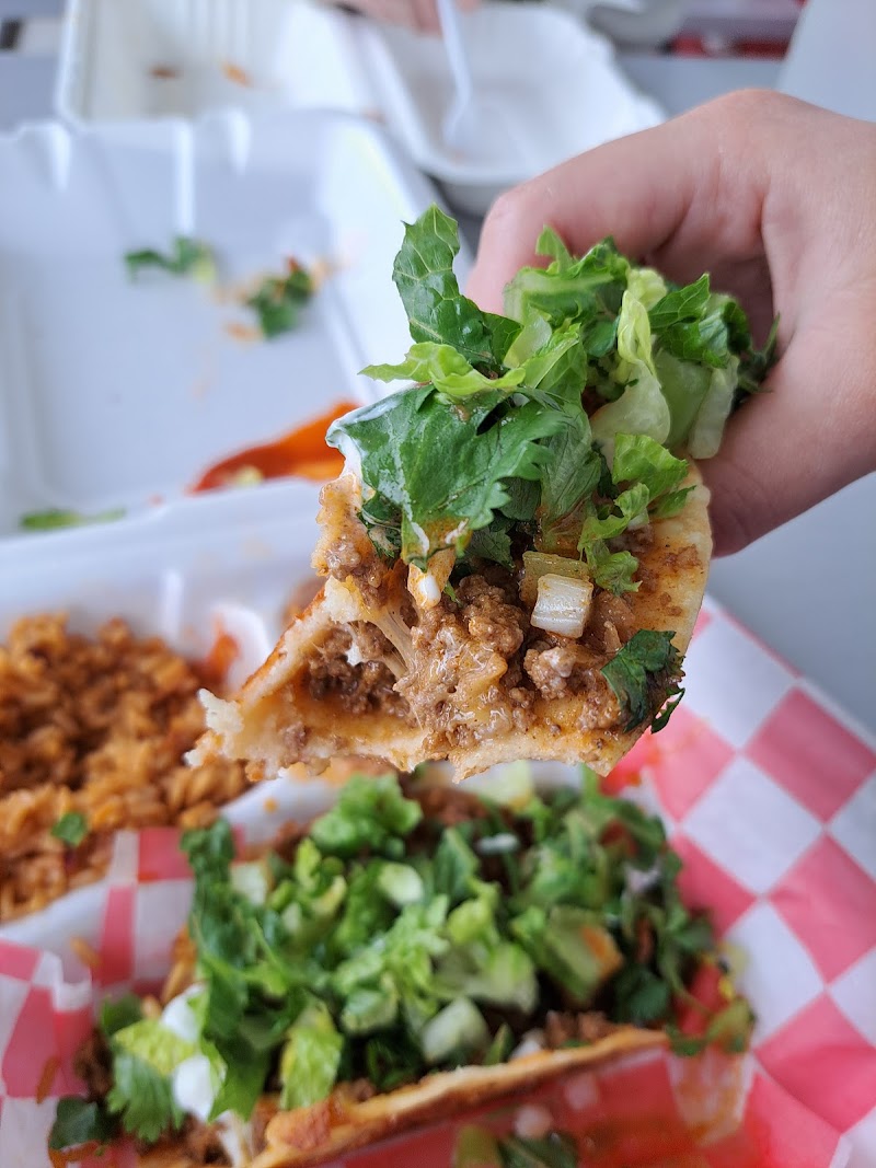 Hand holds a taco with seasoned ground beef, onions, cilantro, and lettuce above a red-checkered basket at Badlands National Park.