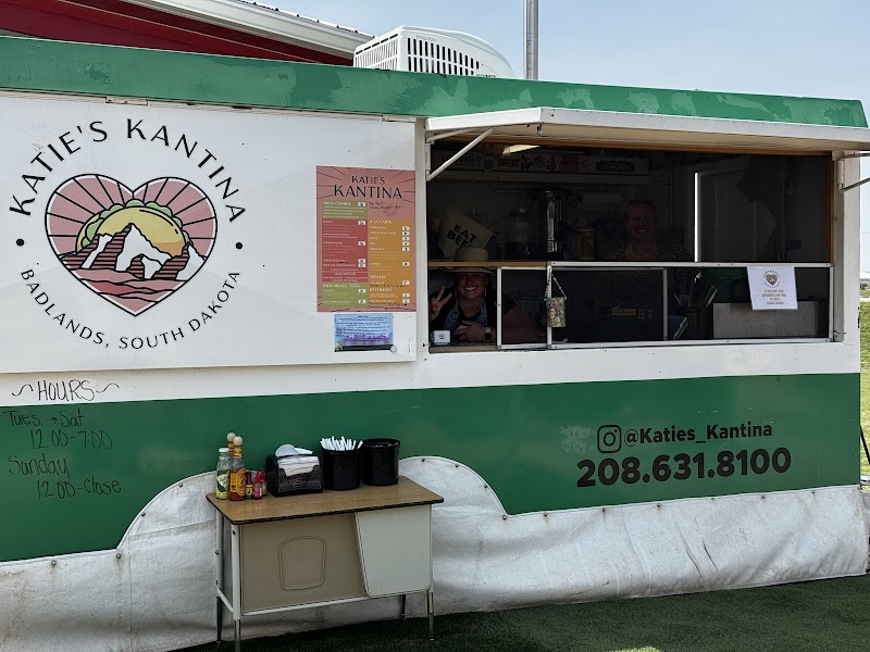 Green and white concession trailer at Badlands National Park with a heart logo, menu board, window service, and condiment table outside.