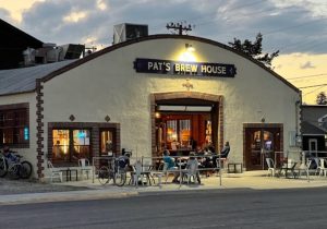 Cream-colored brick-faced restaurant with outdoor seating and warm lights along the street in Yellowstone National Park.