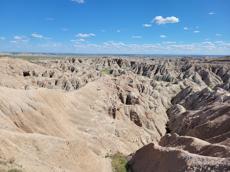 Pinnacles Overlook at Badlands National Park captures sweeping ridges of eroded clay and rock spires stretching to the horizon beneath a clear, sunlit blue sky.