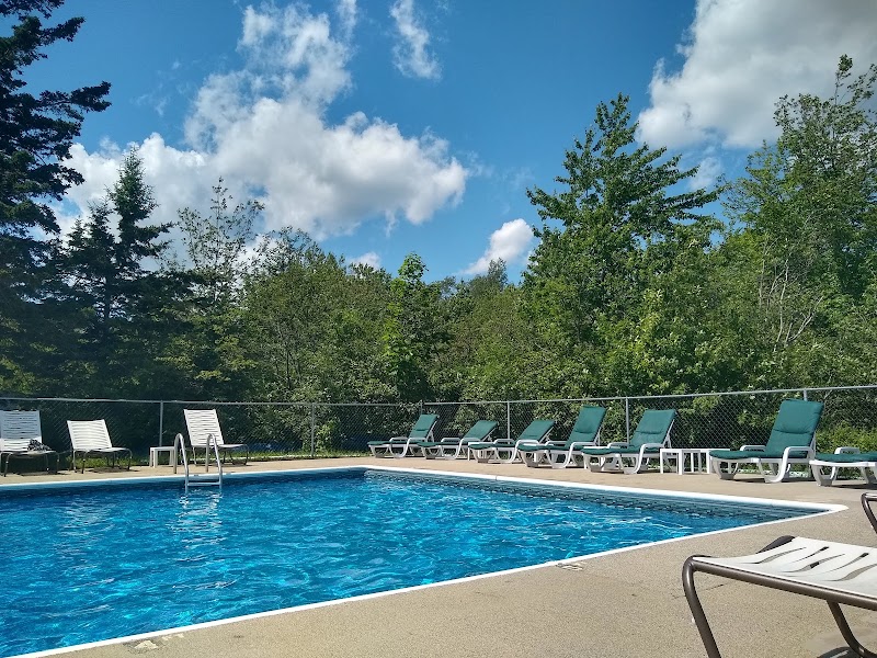 Pool at Narrows Too Campground in Acadia National Park with bright blue water, lounge chairs, and a wooded backdrop.