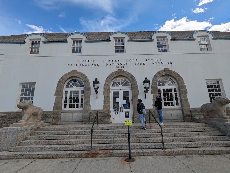 White post office with stone arches and stairs at Mammoth, Yellowstone National Park; two visitors near the entrance.