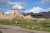 Cedar Pass Campground at Badlands National Park with open grassy sites, picnic shelters, and rugged badlands backdrop under a bright blue sky.