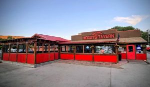 Open-air dining area with bright red wooden panels surrounds a brown tavern-style building in Arches NP under a blue sky.