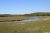 Yellowstone National Park meadow with a winding river, grassy flats, and distant forested hills under a clear blue sky.
