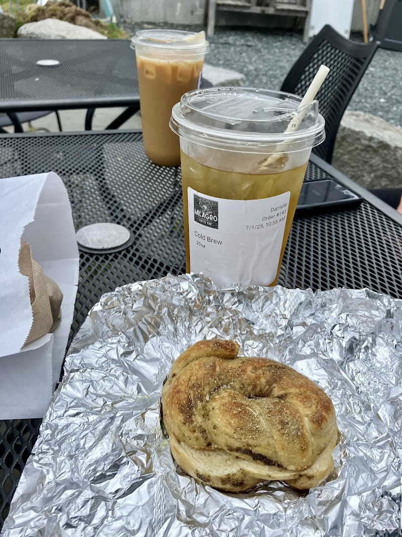 Outdoor metal table at Acadia National Park with two iced coffees in clear cups and a sesame bagel on foil.