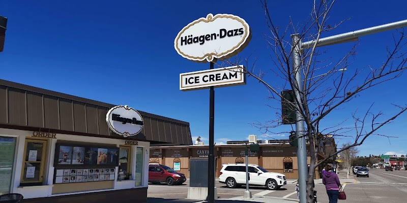Bright blue sky over a small ice cream shop with large signs and order windows, parked cars, and pedestrians in Yellowstone National Park.