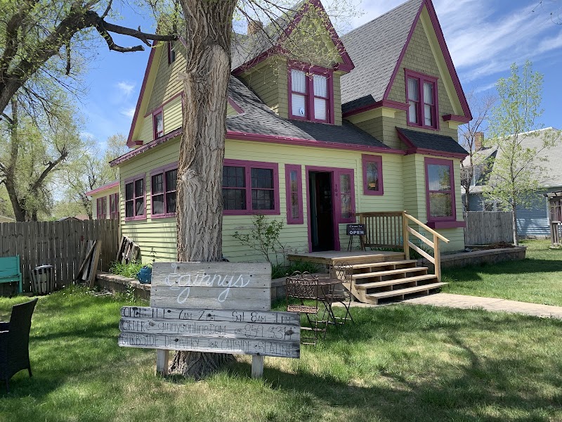 Colorful lime-green house with pink trim beside a tree, wooden steps, and a weathered sign in front in Badlands National Park.