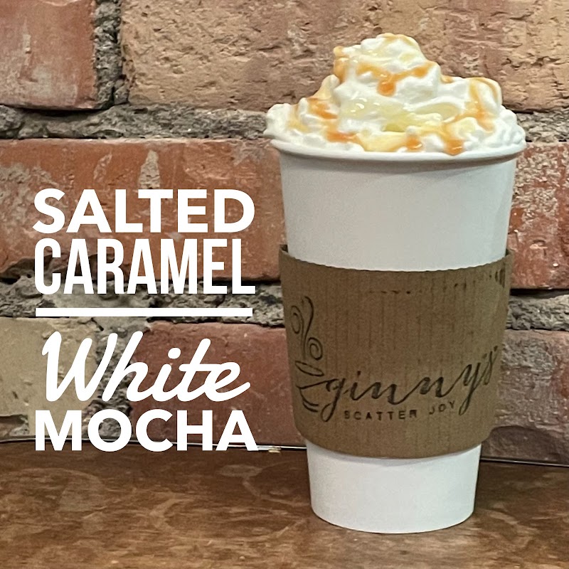 White to-go cup with whipped cream and caramel drizzle, brown sleeve, set against a brick wall in Badlands National Park.