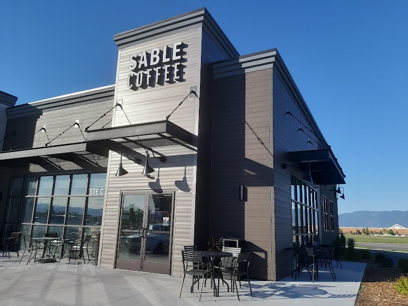 Modern coffee shop exterior with metal siding glass doors and outdoor seating near Glacier National Park