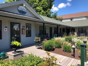 Lacelike lodging office exterior with a covered porch, blooming garden Beds, and a bright blue sky in Acadia National Park.