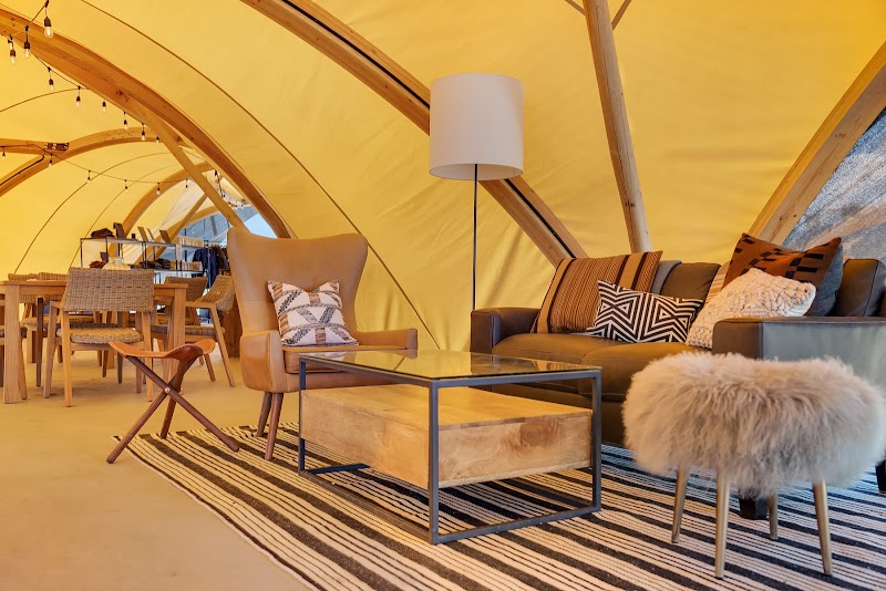 Cozy tent living area inside a yellow canvas shelter with a tan armchair, striped rug, sofa, and fluffy stool in Yellowstone National Park.