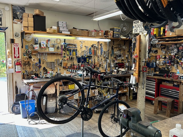 Workshop scene with a black bicycle on a stand, pegboard tool walls, and shelves in Acadia National Park.