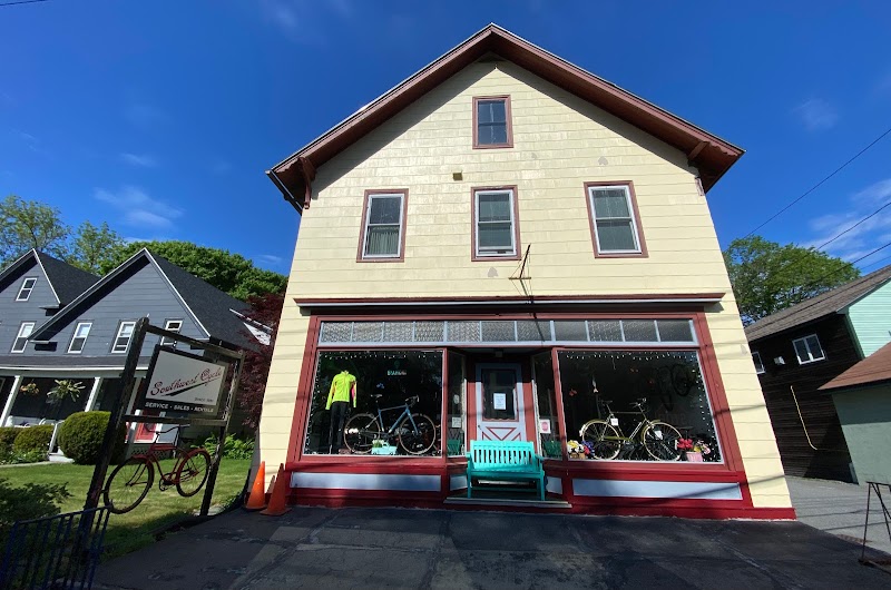Yellow two-story storefront with red trim in Acadia National Park; bicycles in front window and a teal bench.