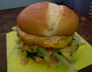 Cheesy burger with lettuce and onions on a yellow napkin, photographed in a casual dining setting.