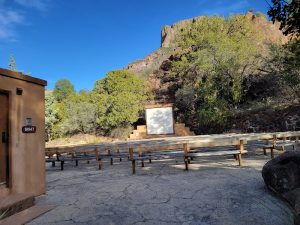 Chisos Basin Campground at Big Bend National Park features wooden picnic tables and a stone landscape under a blue sky.