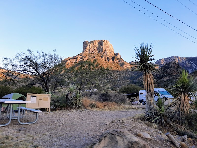 Chisos Basin Campground in Big Bend National Park sits beneath rugged, sunlit peaks with desert scrub and RVs in view.