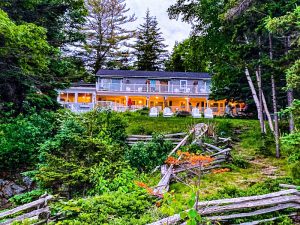 Bay Ledge Inn nestled on a grassy slope with a wraparound porch, surrounded by trees in Acadia National Park.