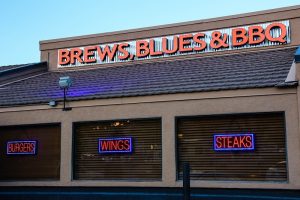 Arches National Park area restaurant storefront with a bold 'BREWS, BLUES & BBQ' sign and neon BURGERS, WINGS, STEAKS.
