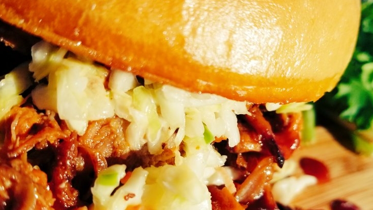 Close-up of shredded pork with cabbage slaw on a glossy bun, resting on a wooden board in Arches National Park.