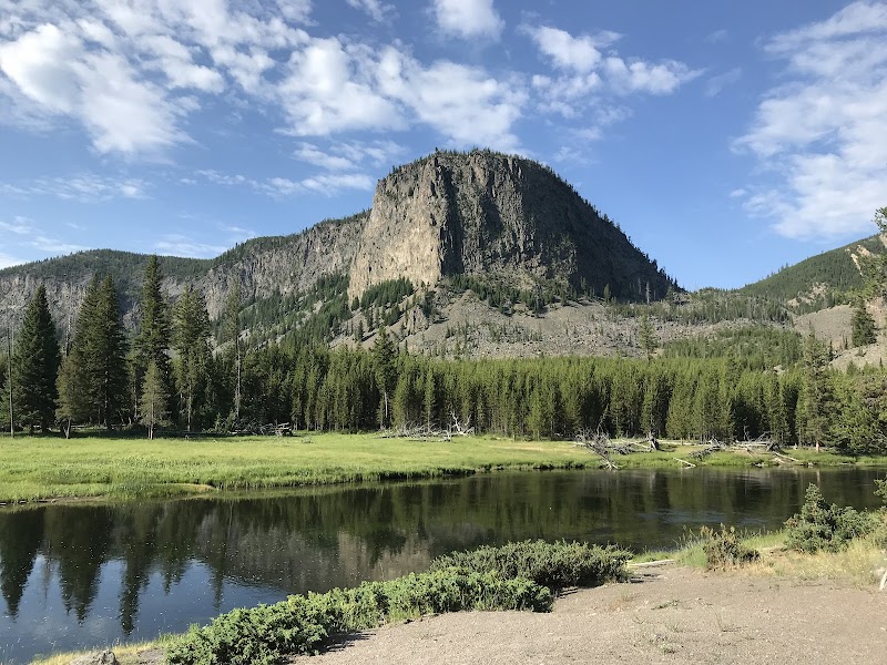 Madison River reflects evergreen trees and a rugged granite hill in Yellowstone National Park.