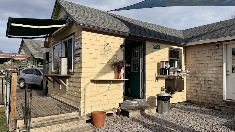 Colorful yellow cafe exterior at Acadia National Park with a green door, outdoor counter, and shade sails.