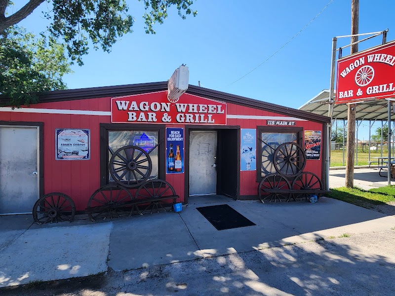 Red wooden bar and grill building with large wagon wheels leaning outside, blue sky above, in Badlands National Park.