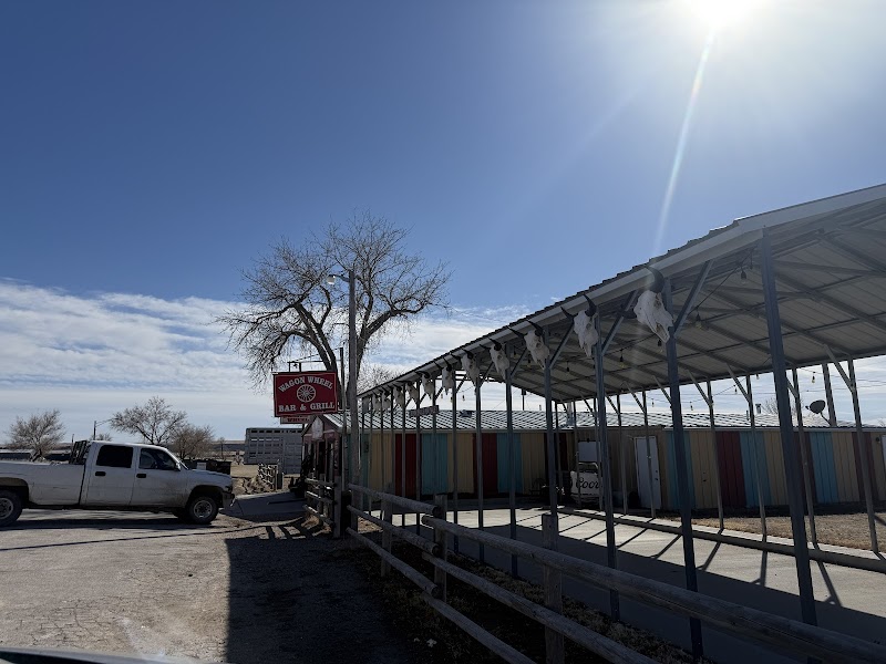 Sunlit parking area at Badlands National Park with a white pickup, a covered walkway, and a colorful row of buildings.
